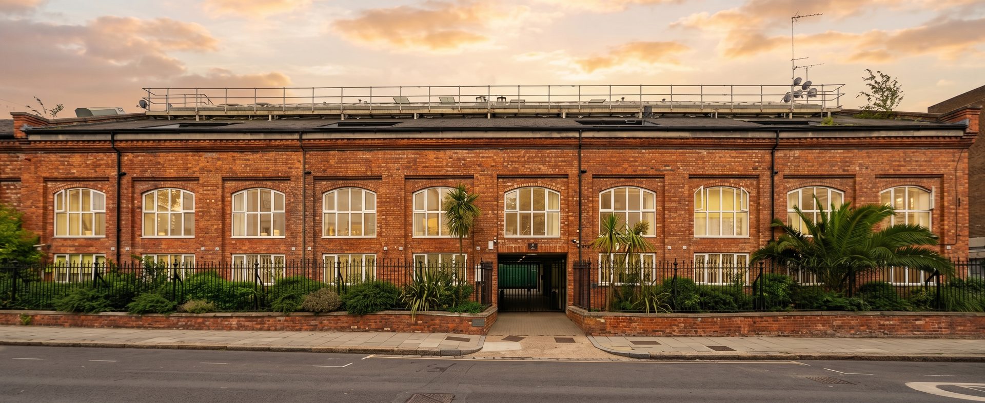 Illustrative golden-hour view of a single-storey London mews-style business centre on a leafy avenue